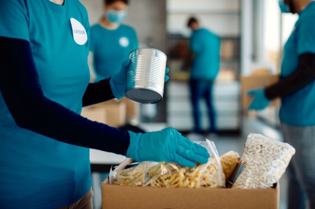 Unrecognizable volunteer packing donated food in cardboard box.